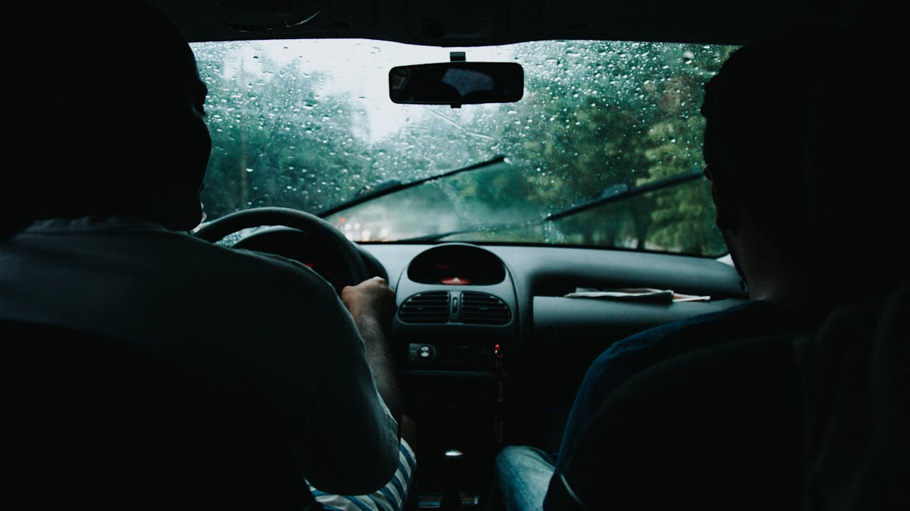 Two people drive through rainy São Paulo streets, wet windshield and raindrops visible.